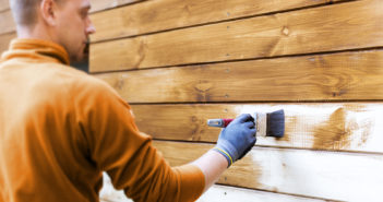 worker painting house exterior with brown wood protective color