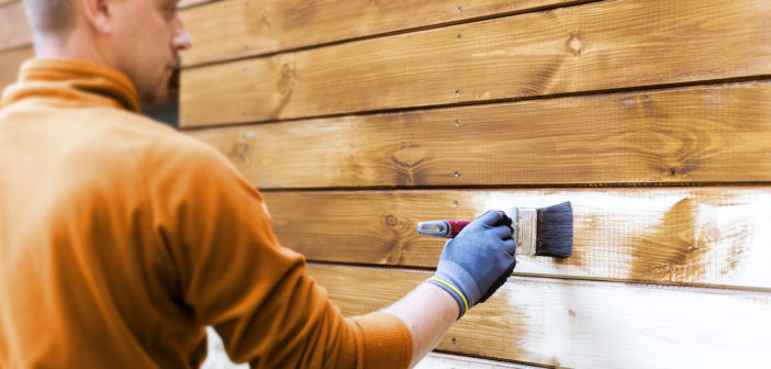 worker painting house exterior with brown wood protective color